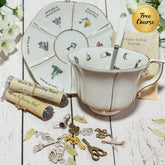 Tea time tarot reading kit displayed on a white wooden surface, including a white ceramic teacup with gold trim and spoon, a matching saucer with illustrated tarot card symbols, a rolled parchment scroll labeled 'Black Tie Reading Will', a small card, and several metal key and lock charms. A gold circular badge reading 'Free Course' appears in the top right.