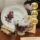 Tea cup and saucer with floral design on a wooden surface, accompanied by tea bags and a card.