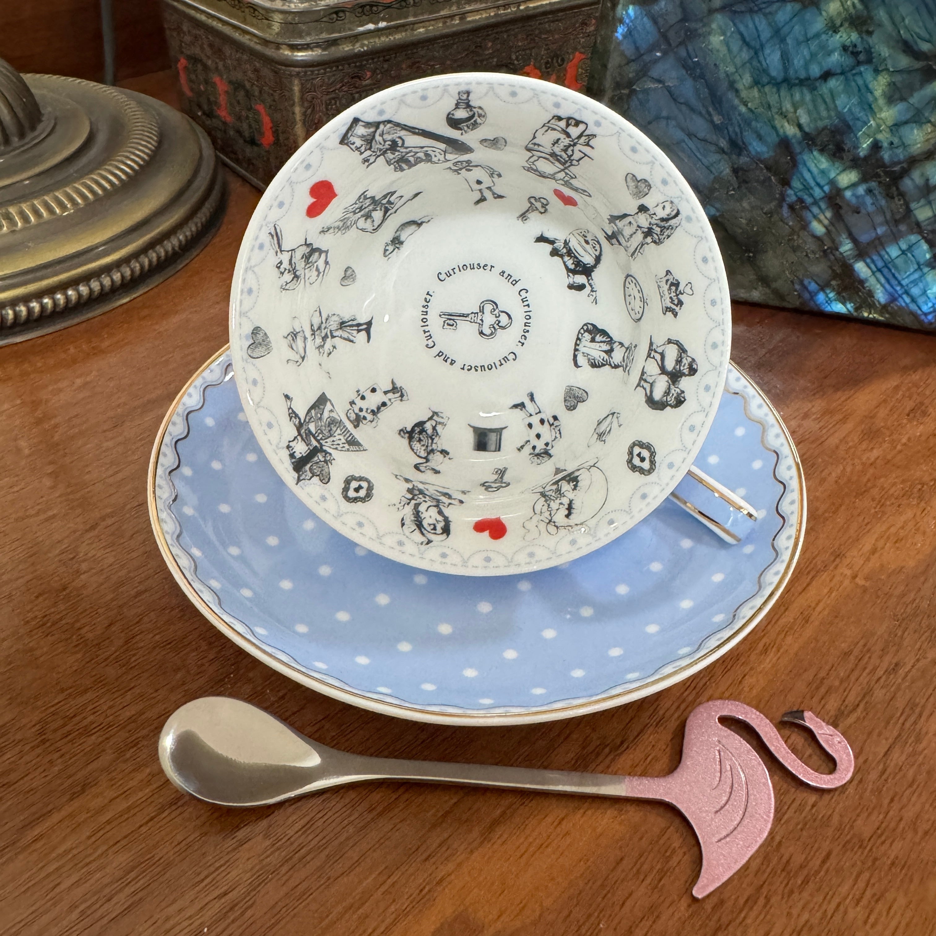 Teacup with decorative design on a wooden surface with a spoon and flamingo-shaped stirrer.