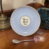 Decorative plate with polka dots and text on a wooden surface with a spoon and decorative item.