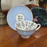 Teacup and saucer set with polka dot design and 'We are all mad here' quote on a wooden surface.