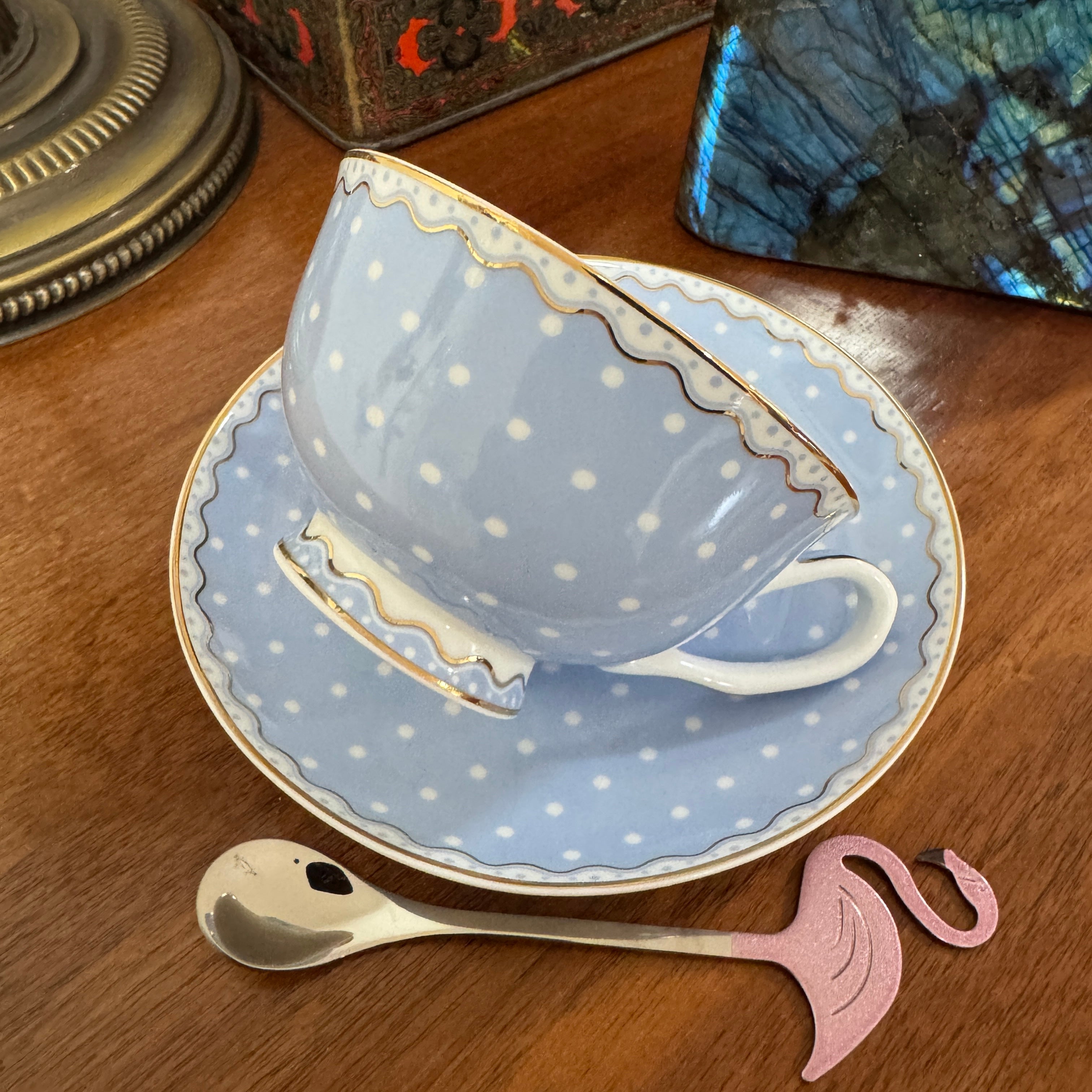 Blue polka dot teacup and saucer on a wooden surface with a spoon and decorative item.
