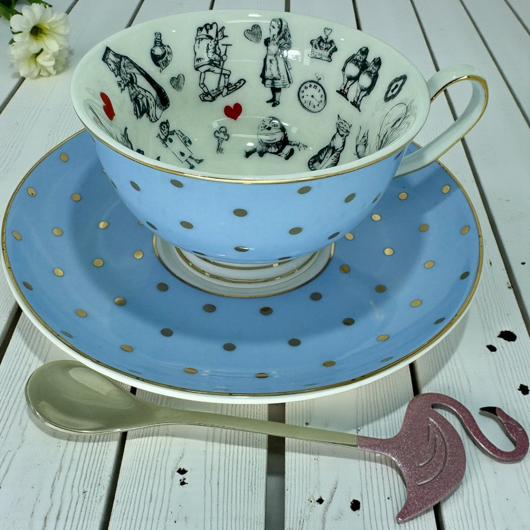Light blue teacup with gold polka dots sitting on its matching saucer, showcasing the black and white Alice in Wonderland imagery inside the rim.