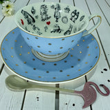 Light blue teacup with gold polka dots sitting on its matching saucer, showcasing the black and white Alice in Wonderland imagery inside the rim.