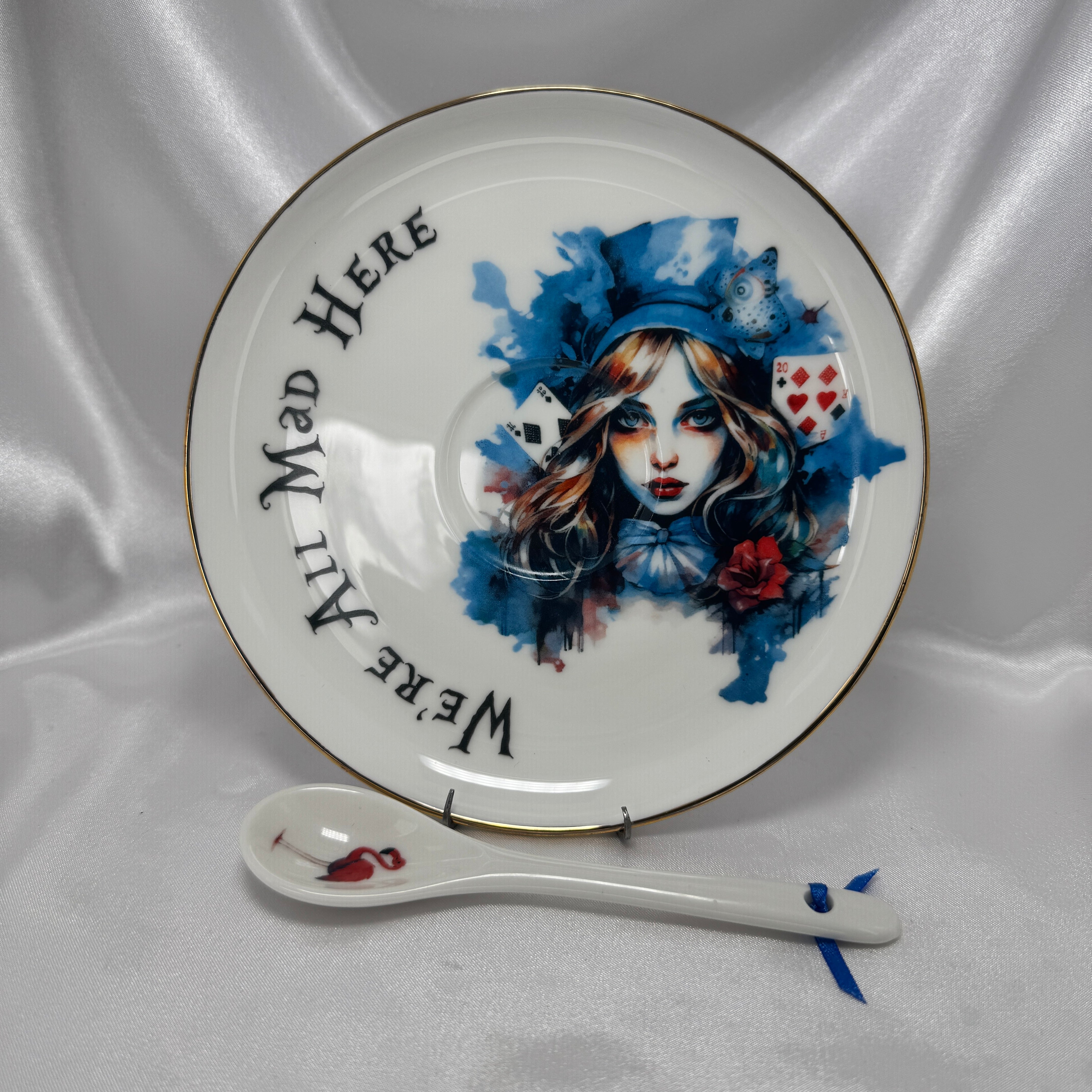 Decorative saucer with  Alice in Wonderland design and a spoon on a white fabric background.