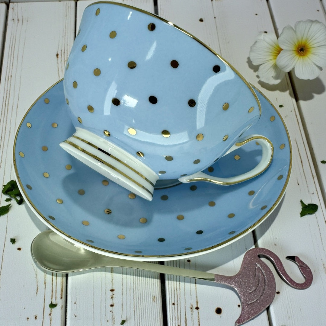 Light blue polka dot teacup and saucer with internal Alice in Wonderland illustrations, showing the handle on the right and a flamingo spoon below