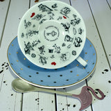 Side view of the blue polka dot teacup tilted on the saucer, showing the internal black and white illustrations of Alice in Wonderland characters