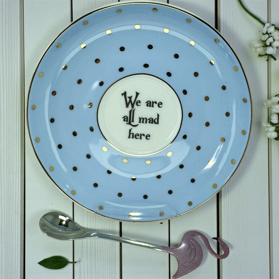 We Are All Mad Here	Close-up top-down view of a light blue saucer with gold polka dots and a central message