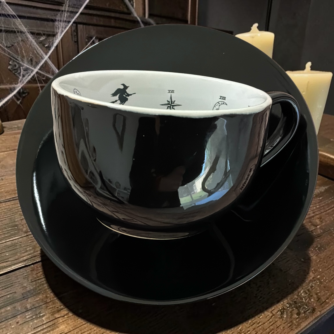 Black Witchy Tarot teacup on its saucer with a witch on her broomstick inside the rim