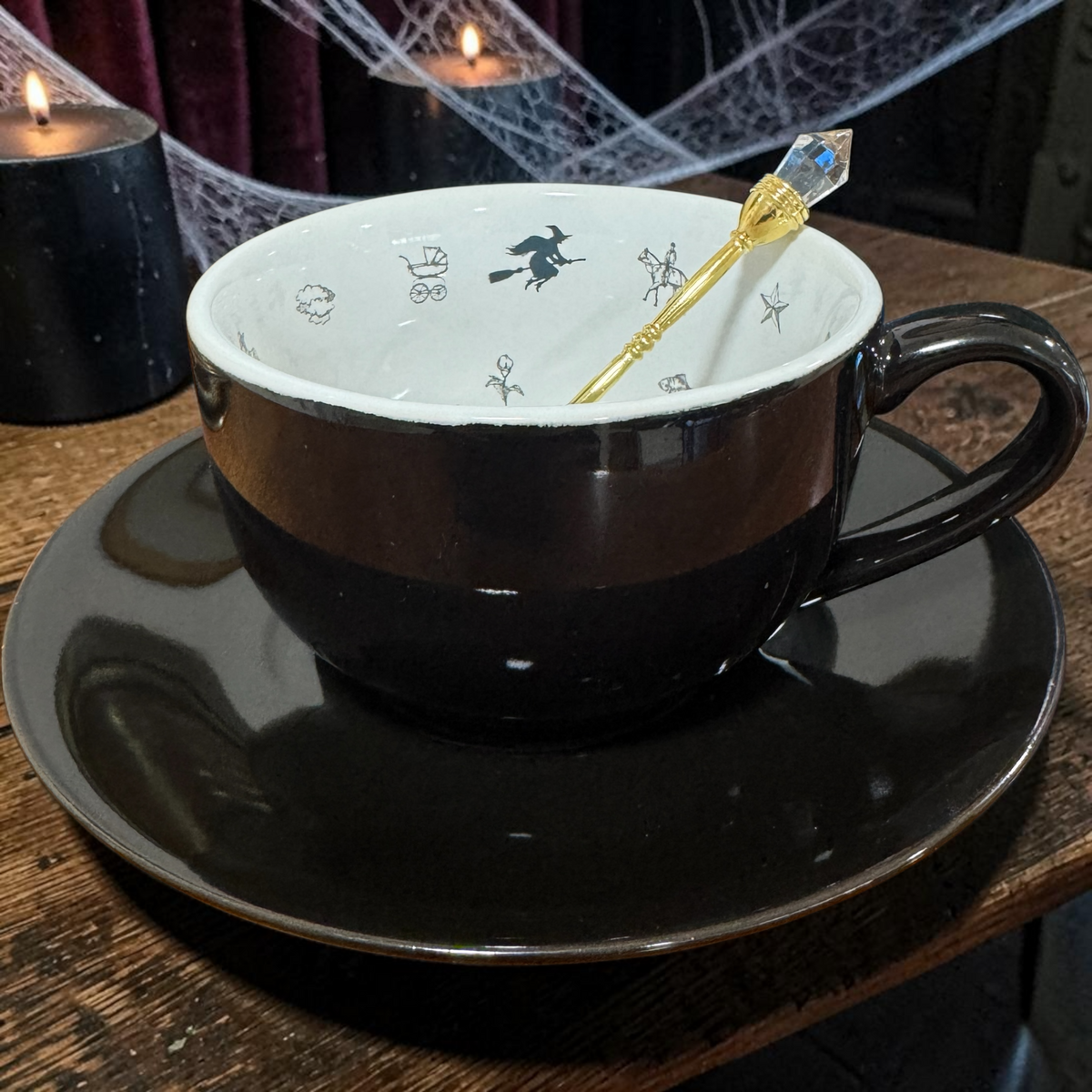 Black Witchy teacup on its jet black saucer with a gold teaspoon resting in the cup