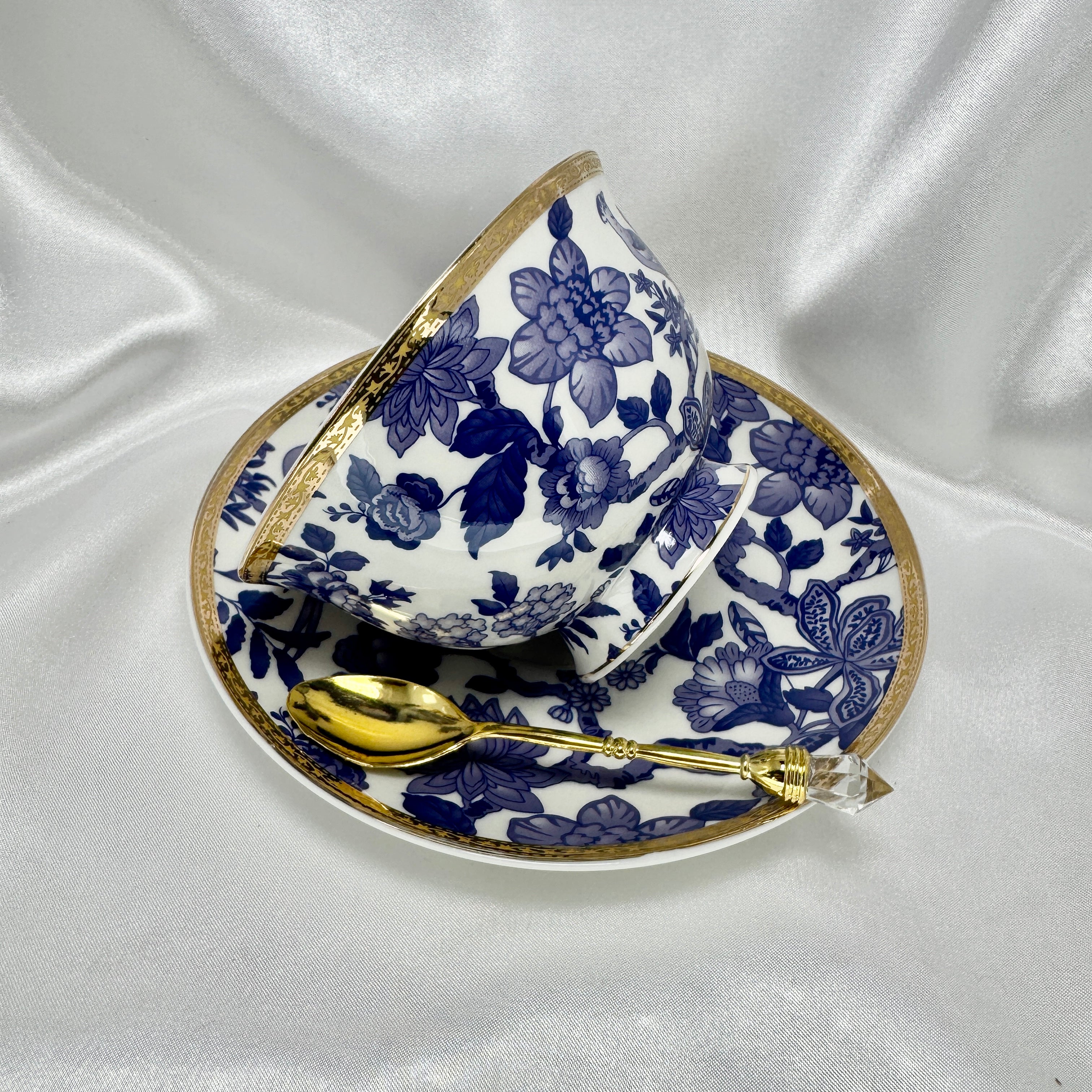 Blue and white teacup sitting on it’s saucer and elegant gold teaspoon. 