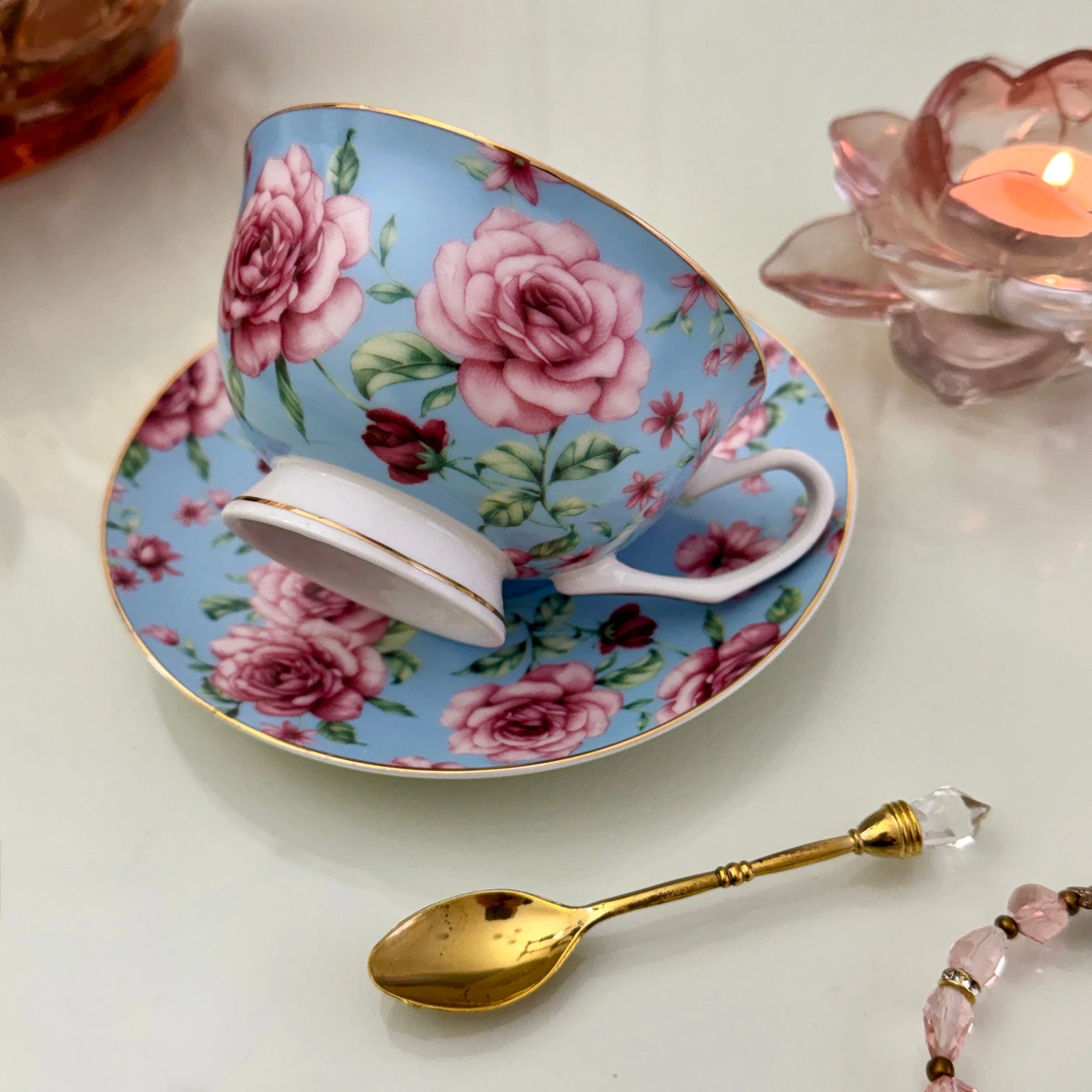 Left side view of blue pink rose floral tasseography teacup tilted on matching saucer with gold crystal teaspoon beside it