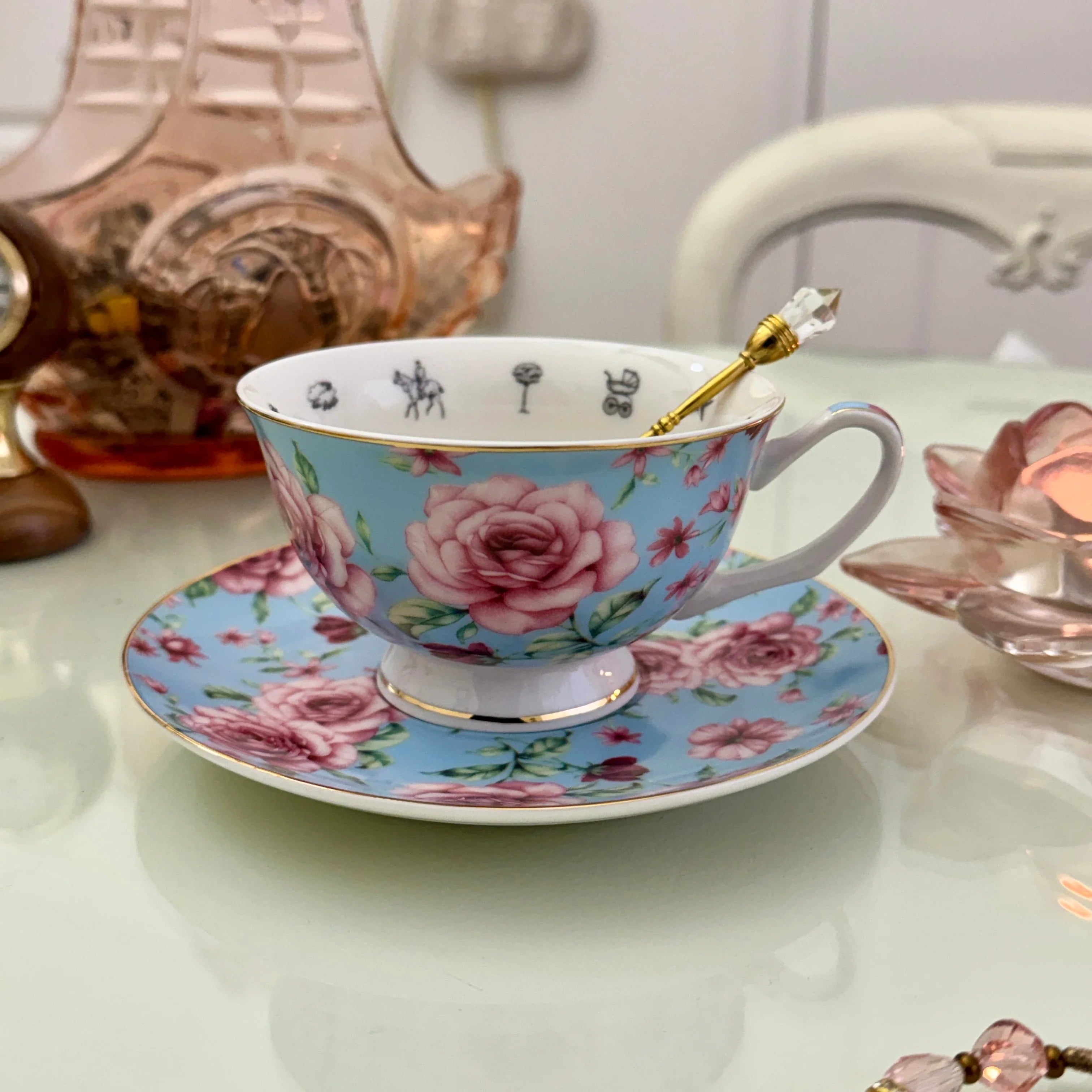 Blue pink rose floral tea leaf reading teacup and saucer set with gold crystal teaspoon resting in cup, upright view showing divination symbols inside