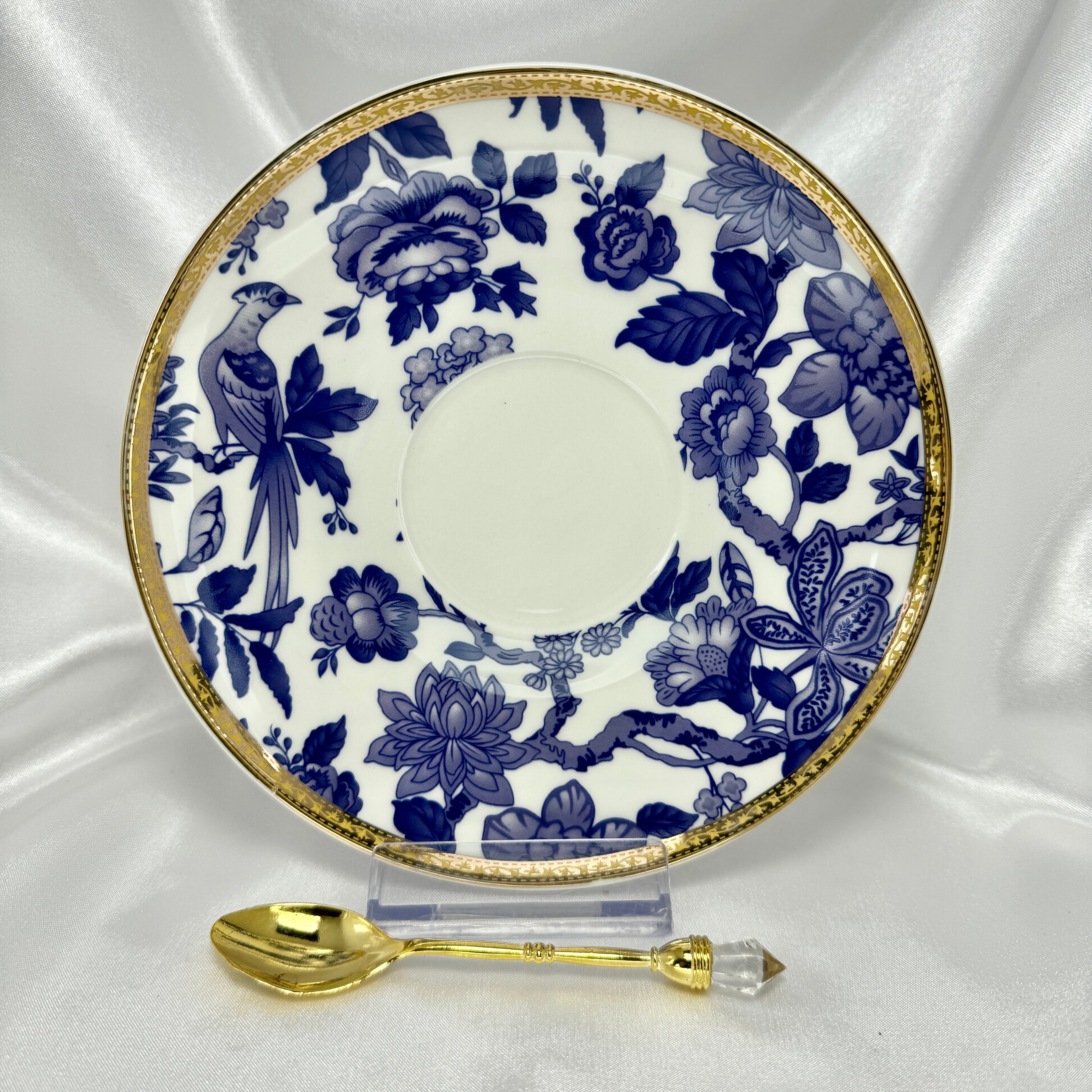 Saucer in blue and white Chinoiserie bird and floral pattern with gold rim, standing upright with a small gold teaspoon.
