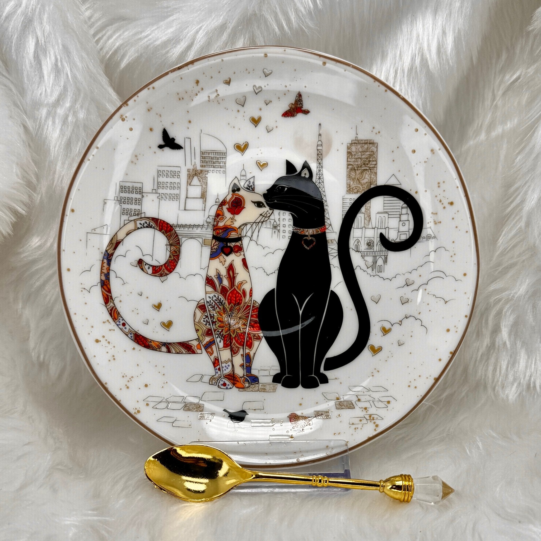 Decorative saucer with two cats and a gold spoon on a white background