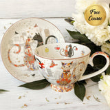 Decorative teacup and saucer with cat designs on a white wooden surface with flowers.