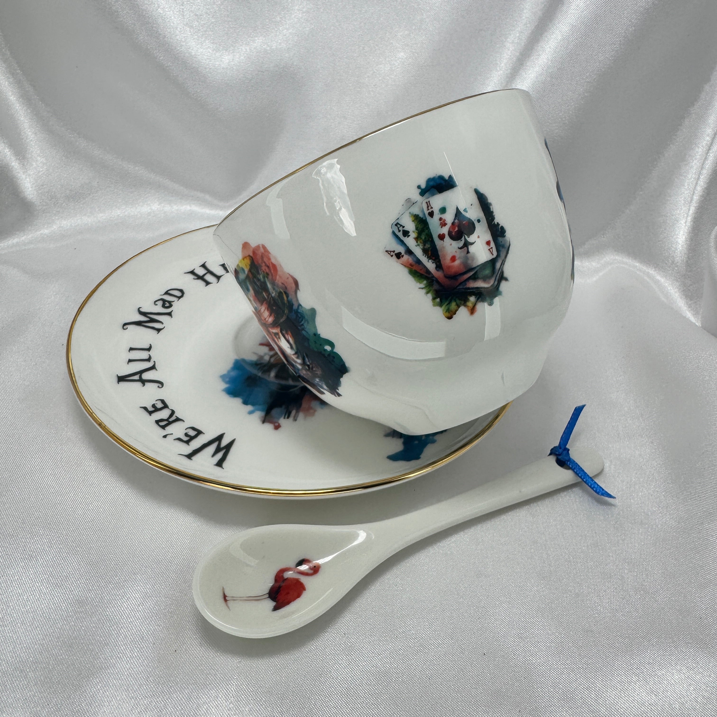 Teacup with decorative design, saucer with text, and spoon on a white fabric background