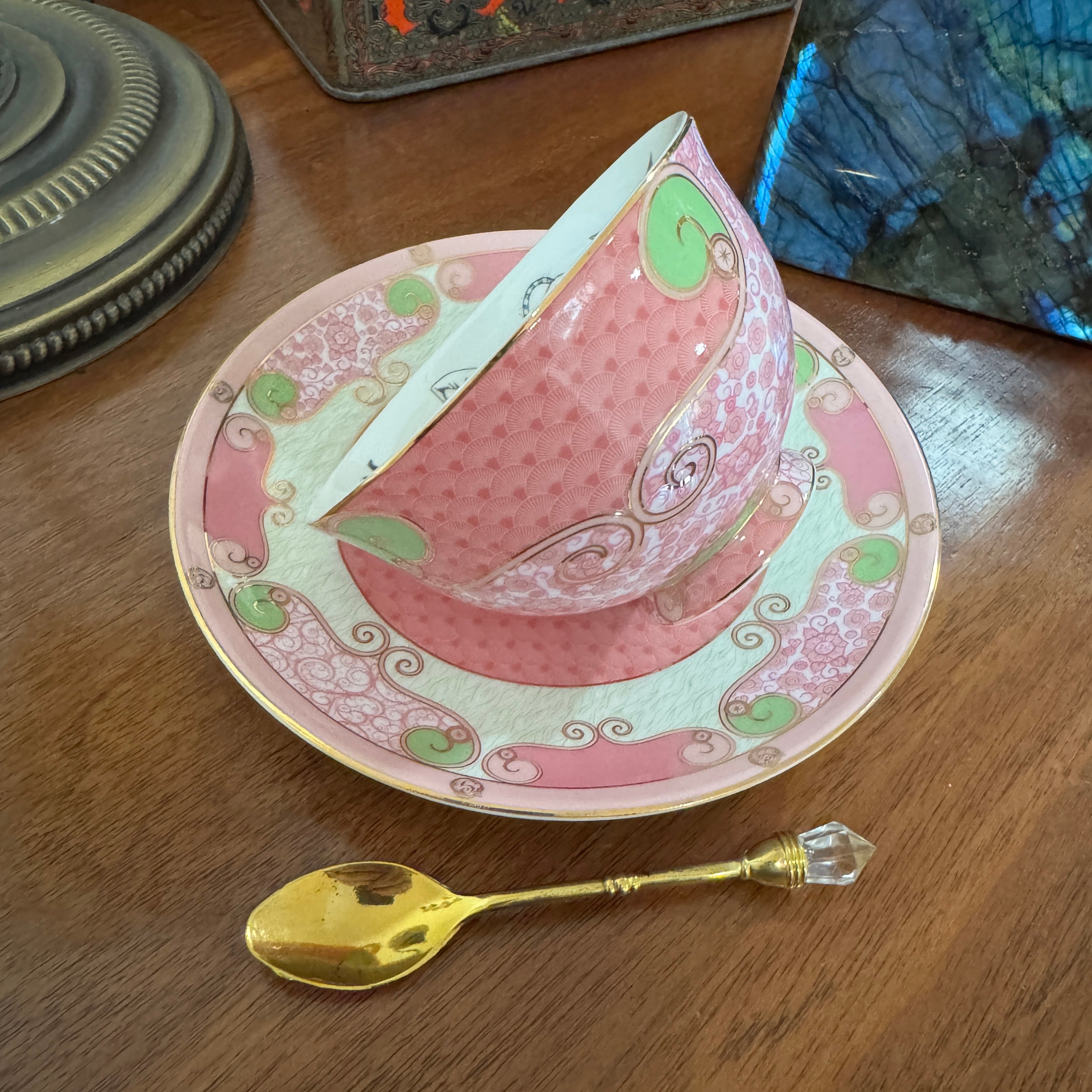 Decorative pink teacup and saucer with a gold spoon on a wooden surface