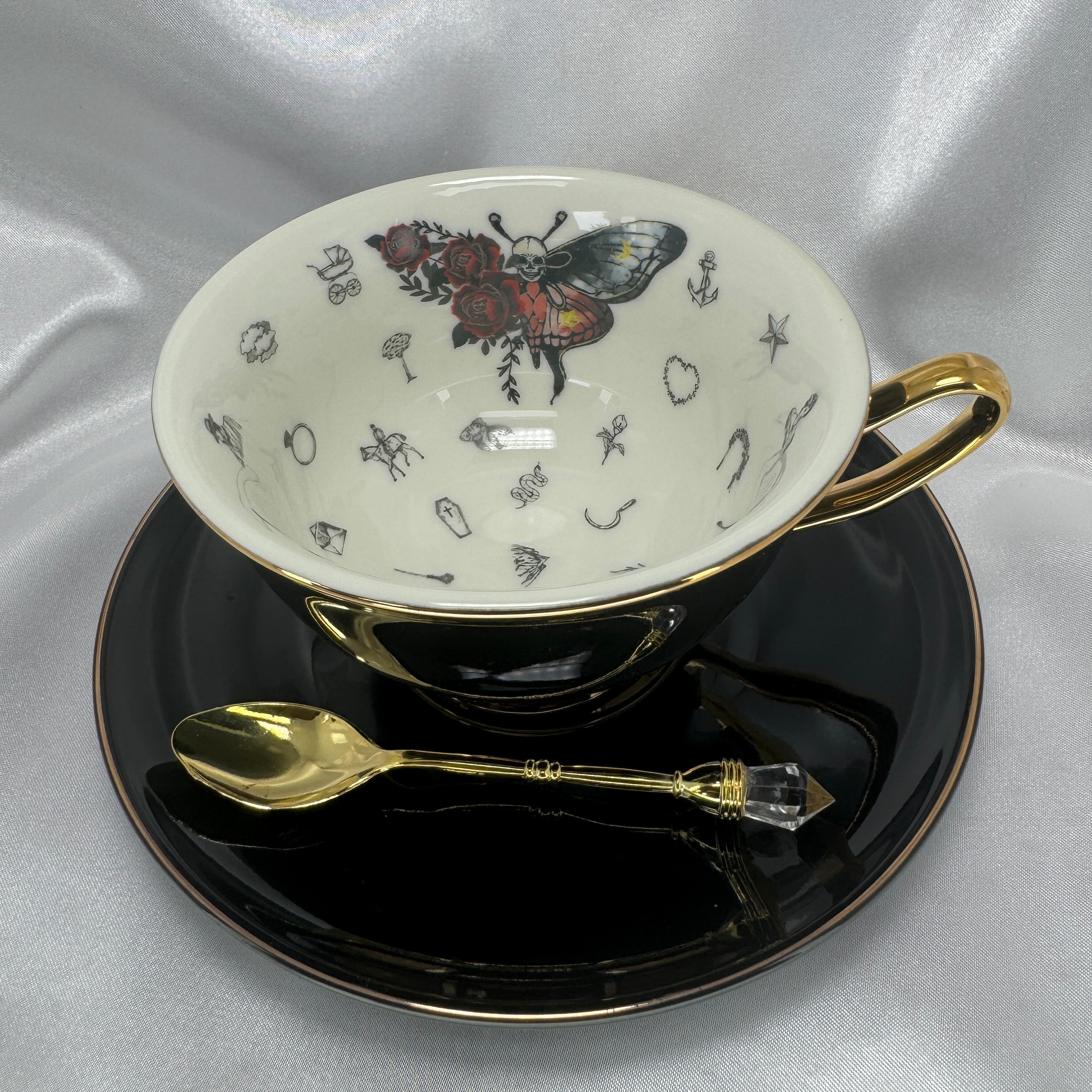 Detailed close-up of the teacup interior showing the skull-moth, red roses, and various black symbols for tea-leaf reading.