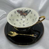 Detailed close-up of the teacup interior showing the skull-moth, red roses, and various black symbols for tea-leaf reading.