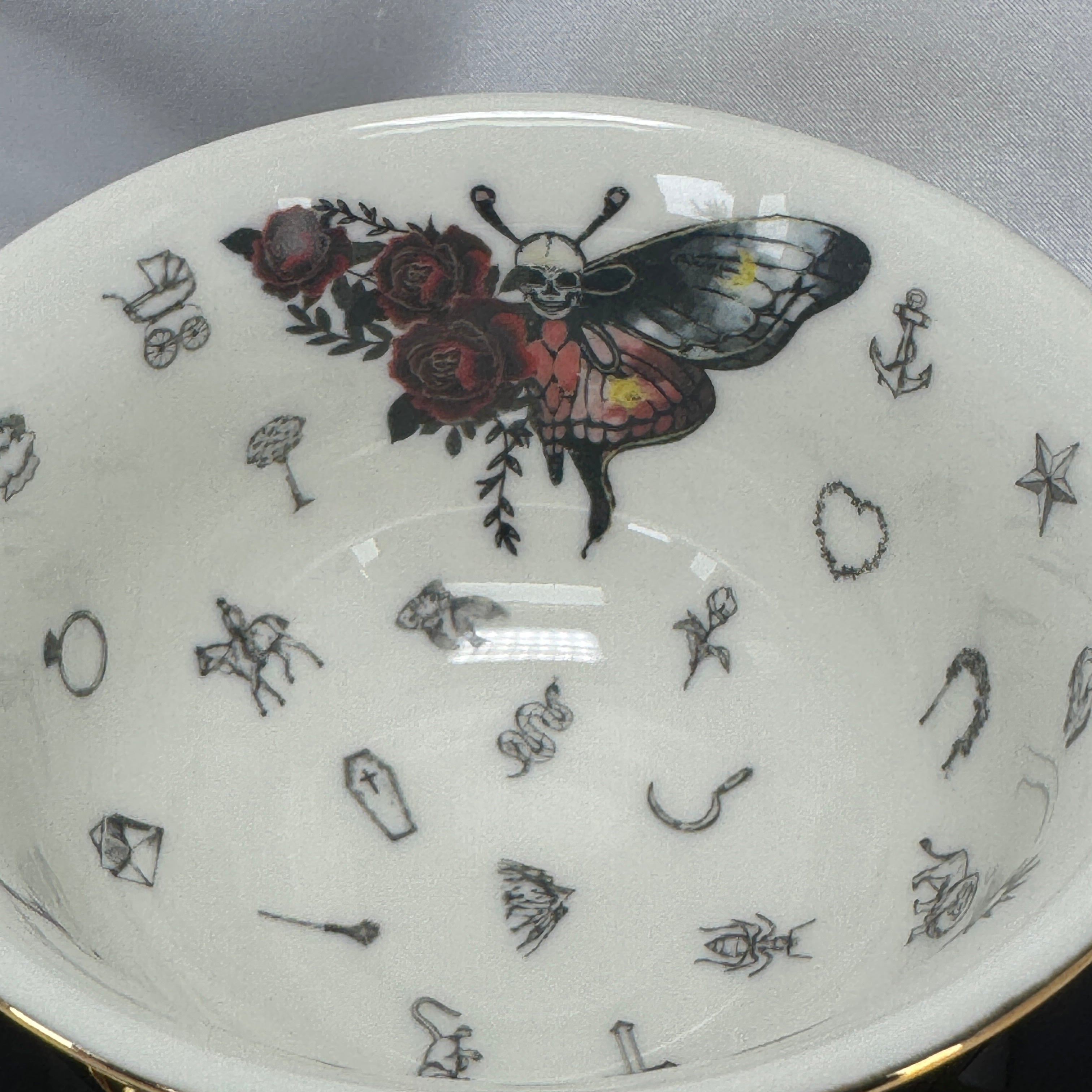 Teacup resting on its side on a saucer, showing the shiny black exterior and gold handle, highlighting the sleek design.