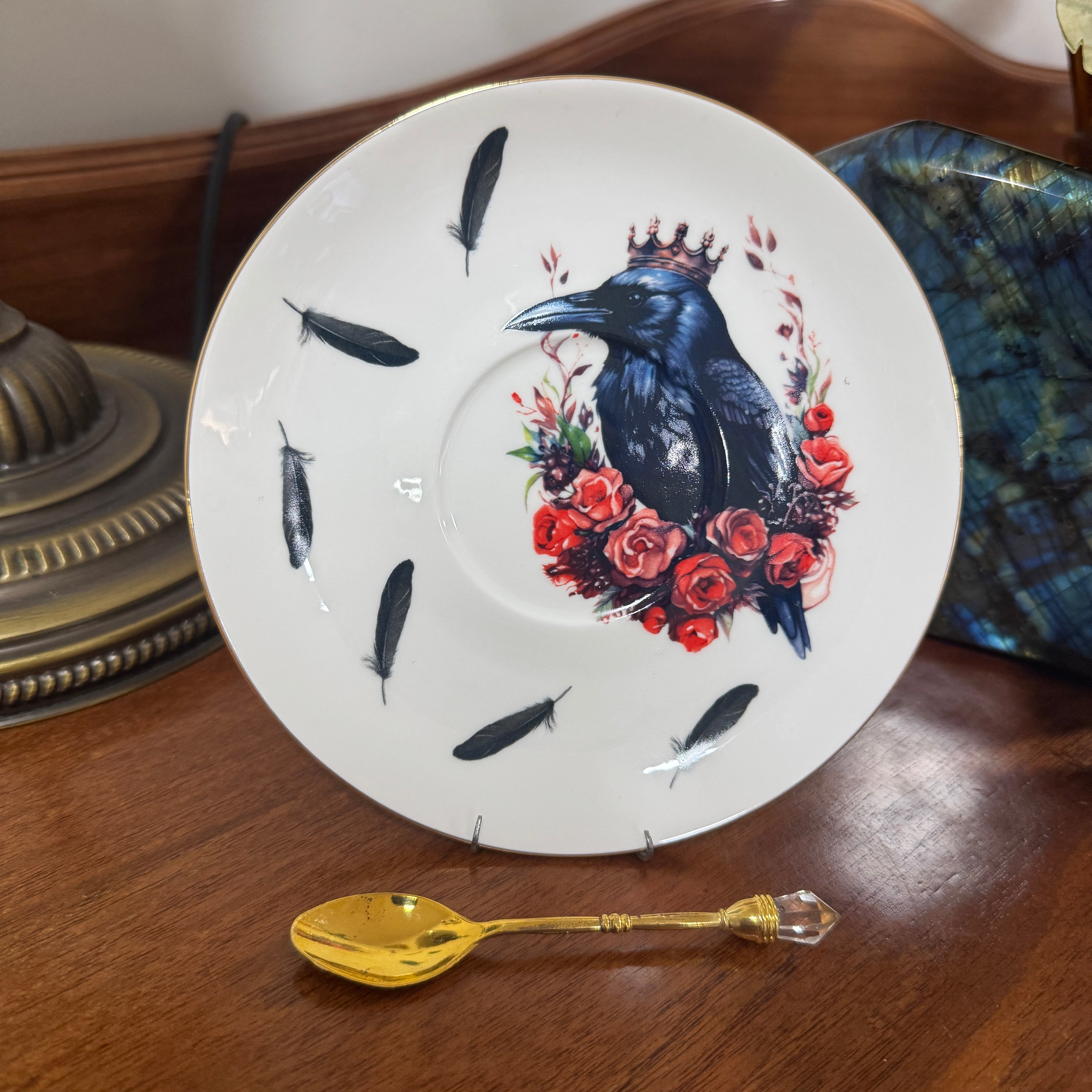 Decorative plate with a crow and floral design on a wooden surface with a gold spoon.