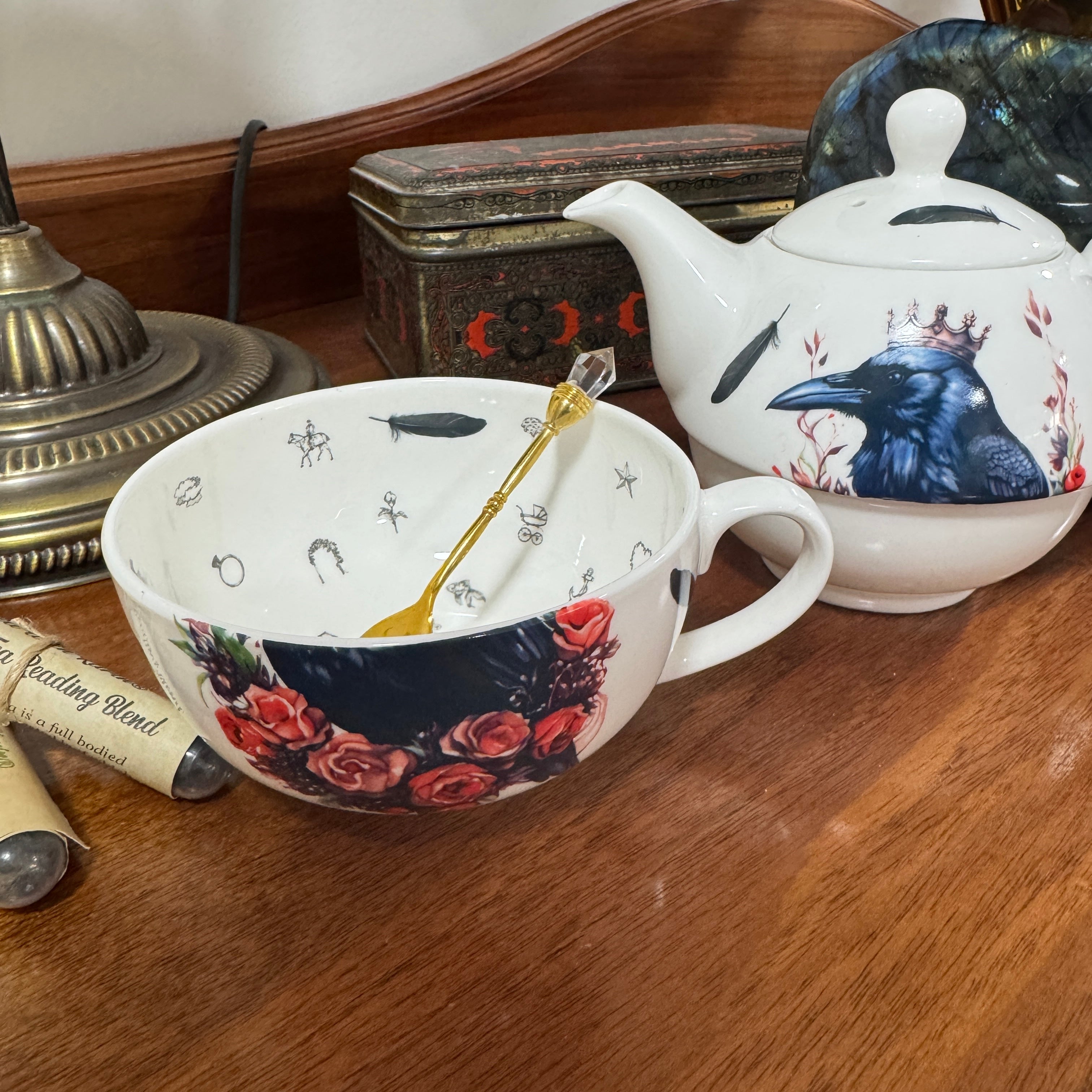 Decorative teacup and teapot with floral and bird designs on a wooden surface.
