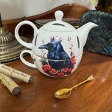 Teapot with a crow design on a wooden surface with tea packaging and a spoon.