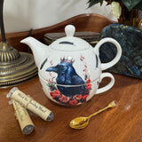 Teapot with crow design, gold spoon, and tea packages on a wooden surface