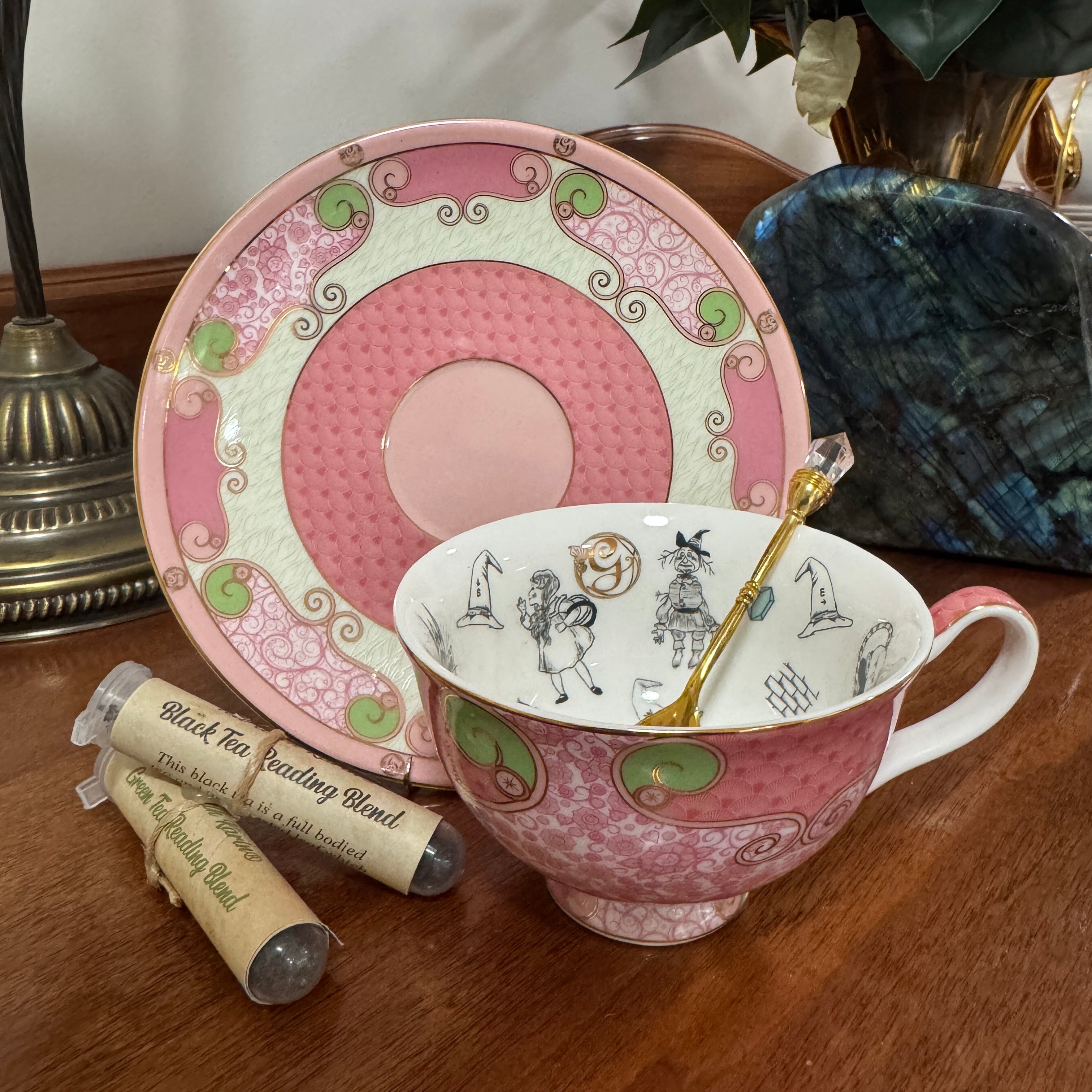 Decorative pink teacup and saucer with a spoon on a wooden surface, next to tea bags.