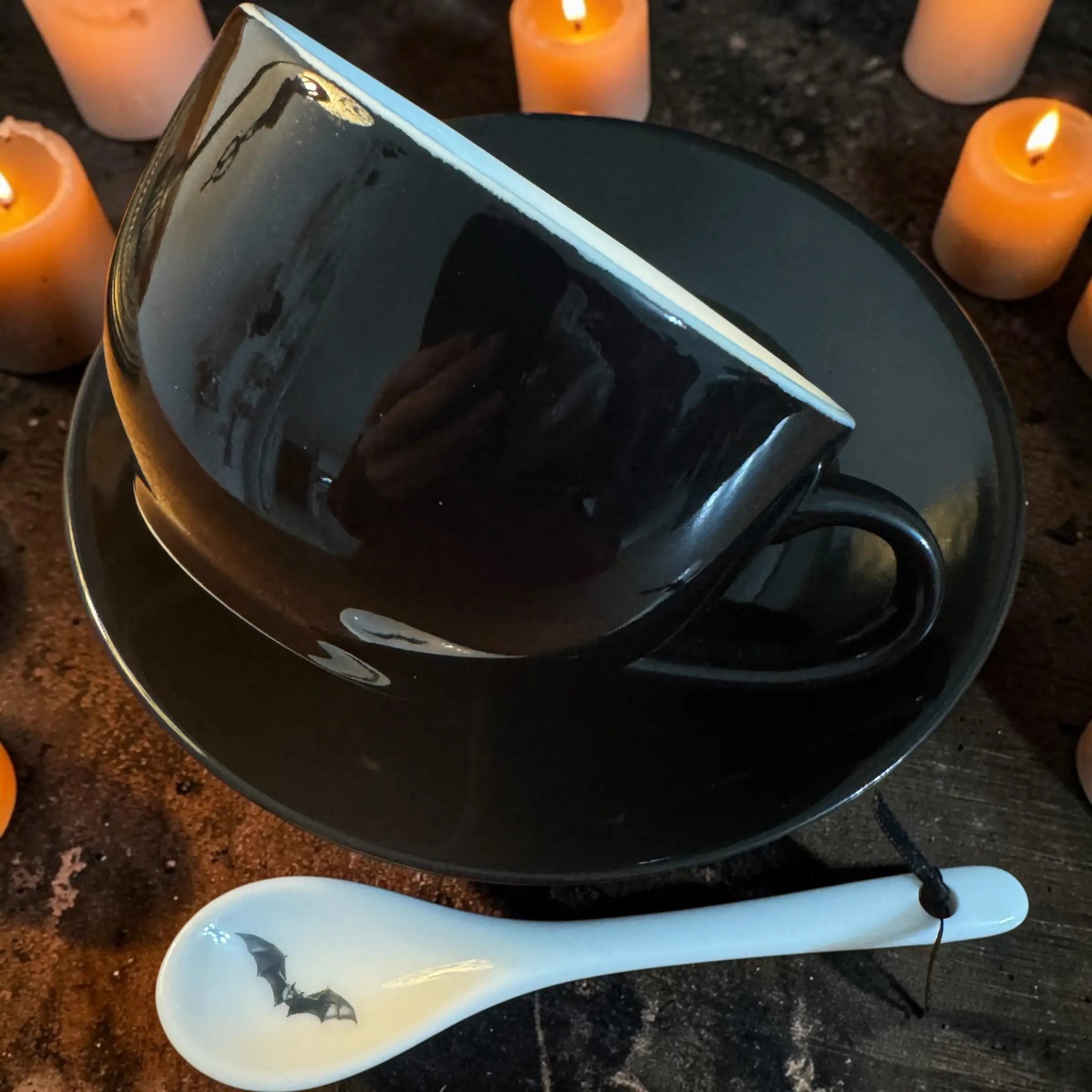 Side view of the jet black Halloween teacup on its saucer with the white china bat spoon
