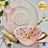 Pink teacup with gold spoon and saucer on a wooden surface with flowers