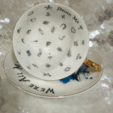Whimsical Alice in Wonderland tea set with gold-accented teacup, saucer, and teaspoon, featuring vivid symbols inside the cup, perfect for tea leaf reading and divination