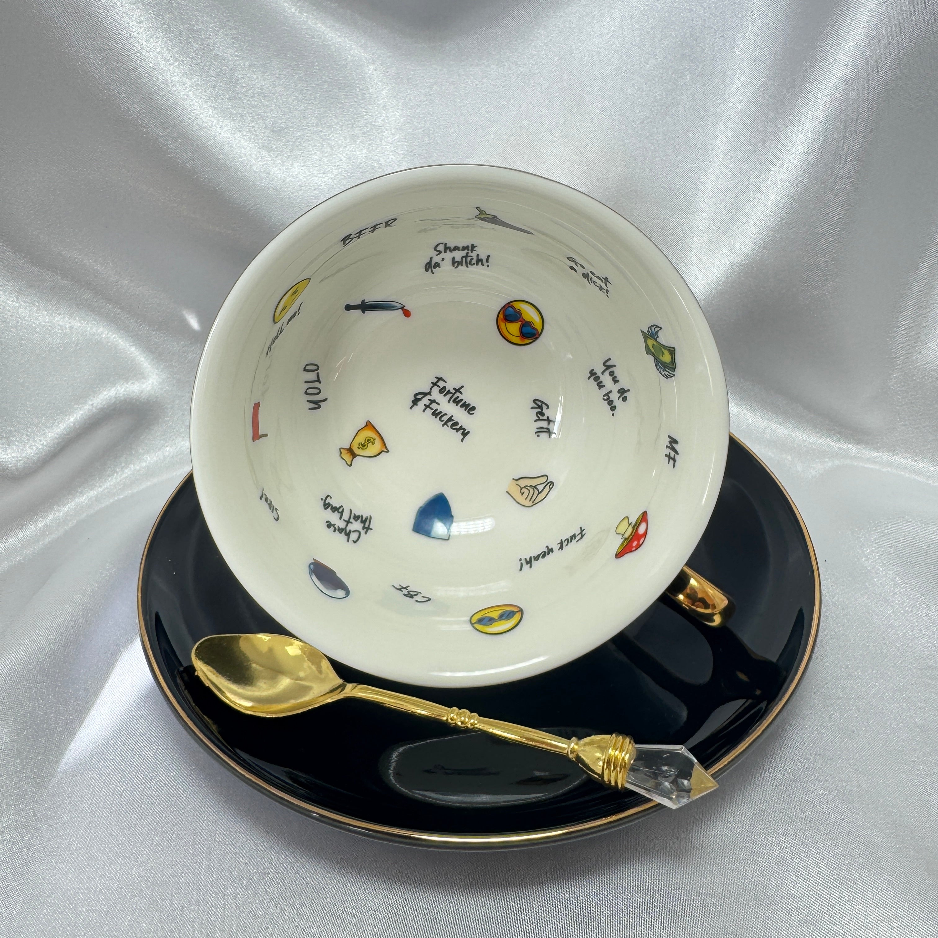 Teacup on its side showing the white interior printed with various emojis and profanity-laced fortune-telling words.