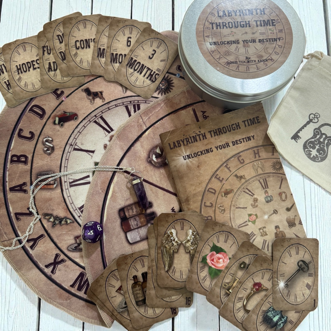 Overhead view of the Labyrinth Through Time charm casting kit, featuring the large alphabet and time clock mat, the storage tin, the key motif pouch, the guidebook, and the pendulum necklace used for guidance.