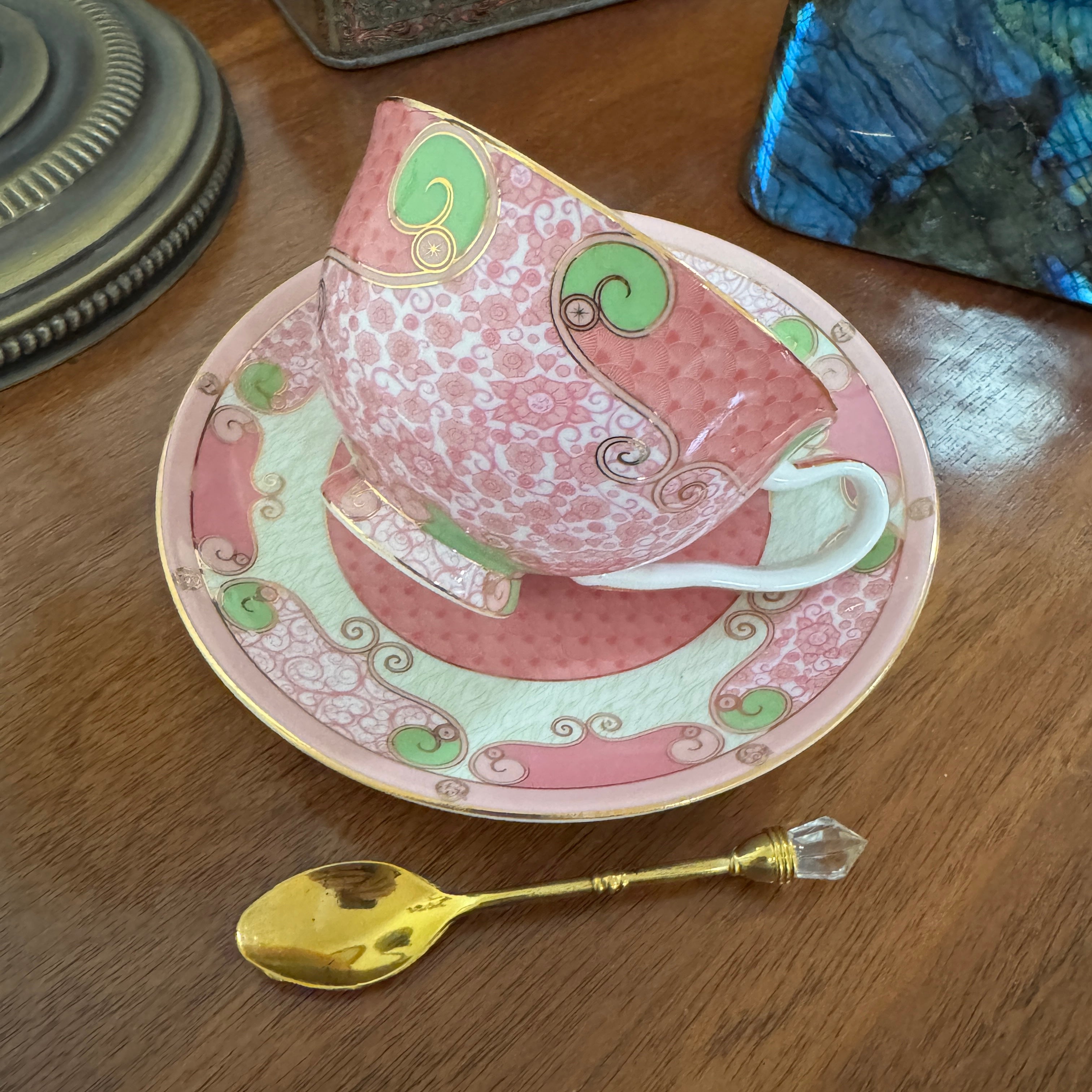Decorative teacup and saucer with a gold spoon on a wooden surface
