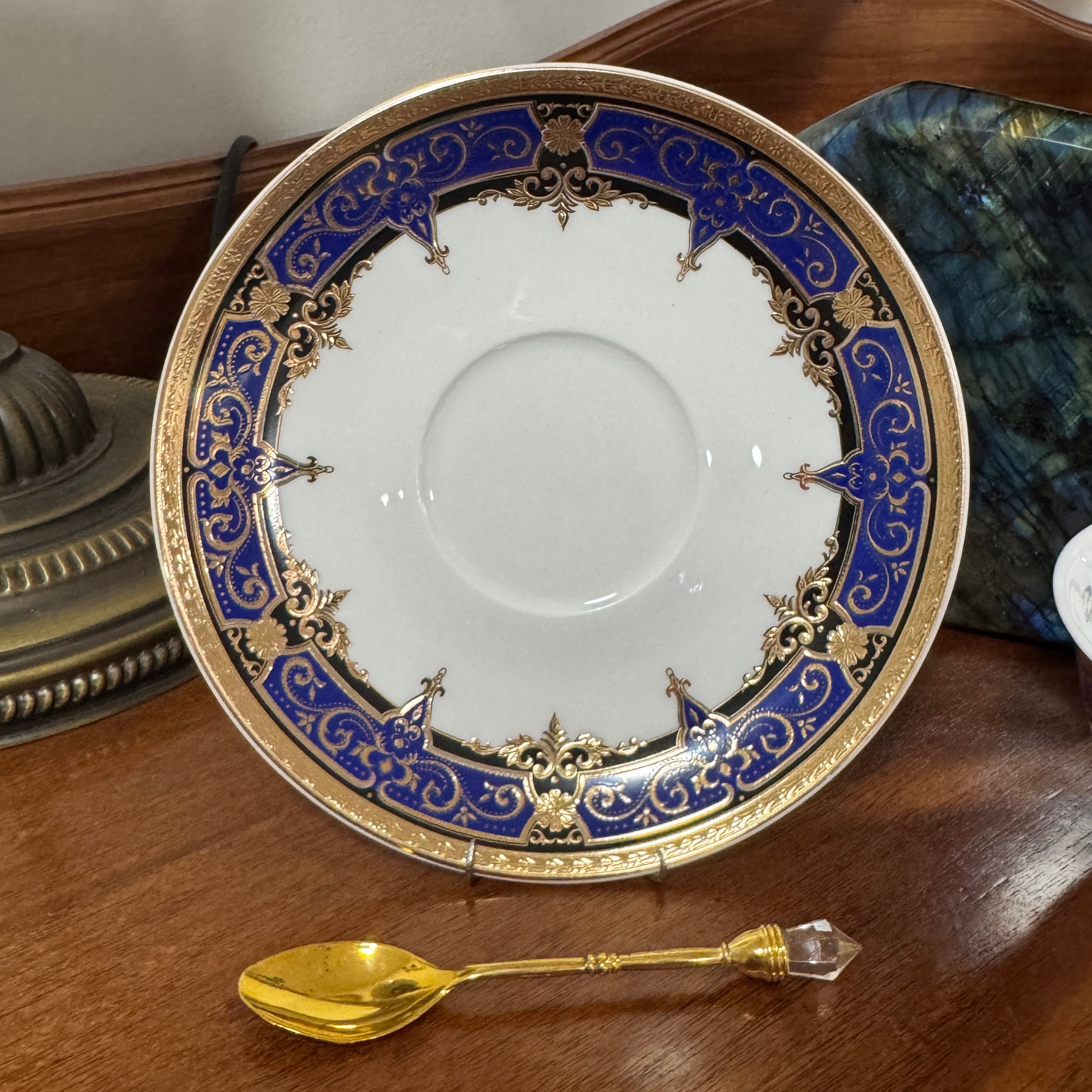Decorative plate with blue and gold rim on a wooden surface, accompanied by a gold spoon.