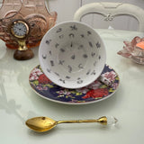 Inside view of navy red rose floral tasseography teacup face-up showing all 32 printed tea leaf reading divination symbols, resting on matching saucer with gold crystal teaspoon