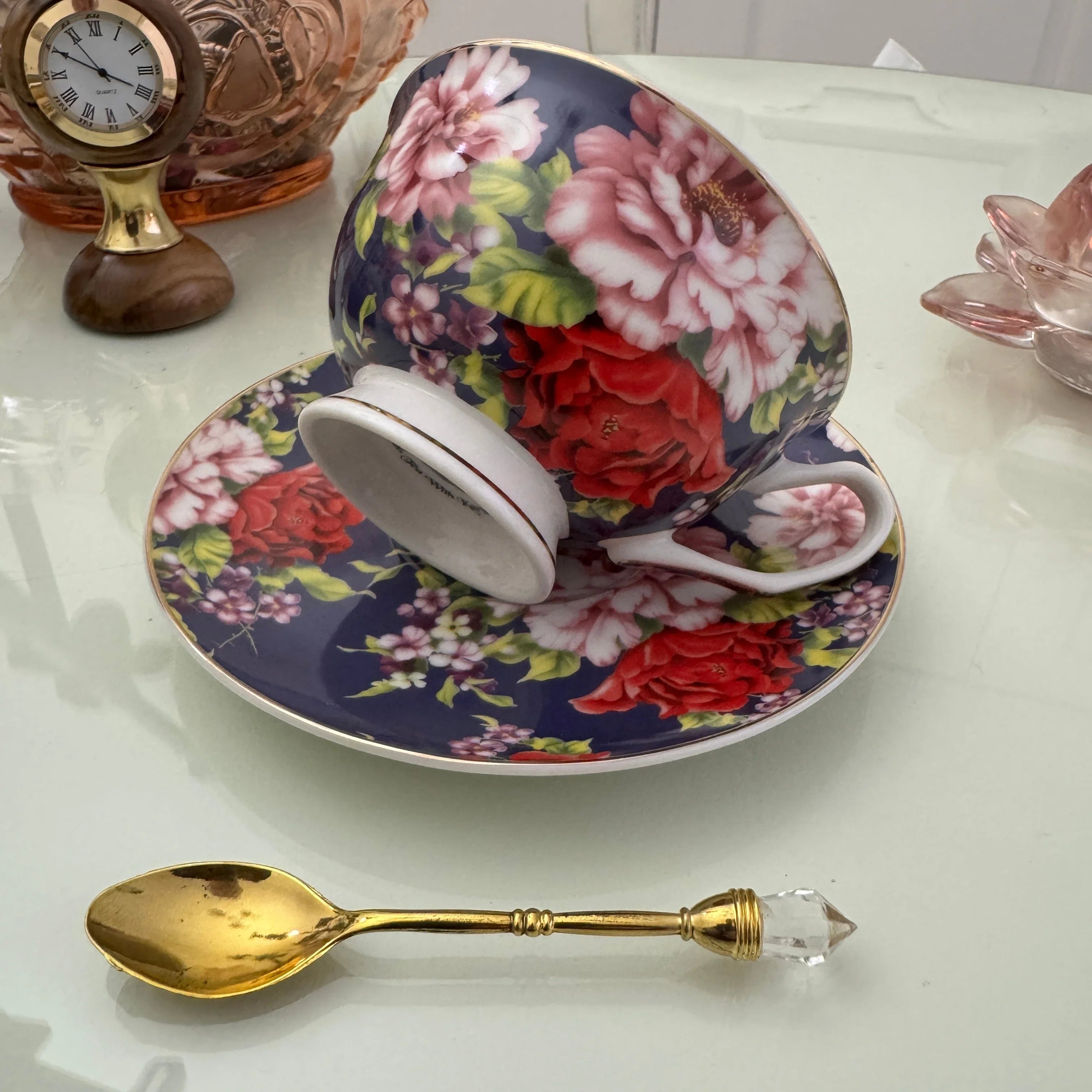 Left side view of navy red rose floral tasseography teacup tilted on matching saucer with gold crystal teaspoon beside it