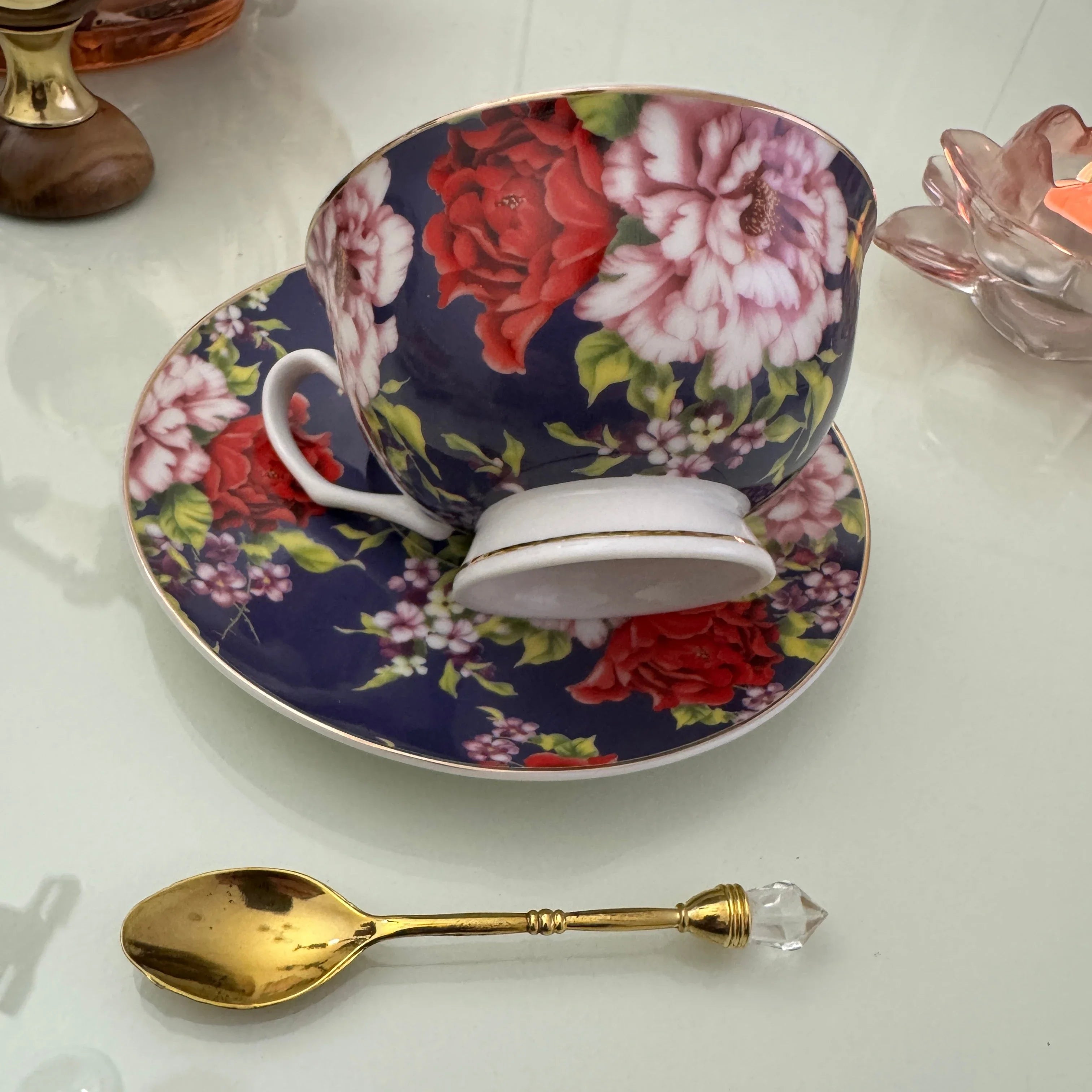 Right side view of navy red rose floral tea leaf reading teacup tilted on matching saucer with Tea With Karin stamp visible on base