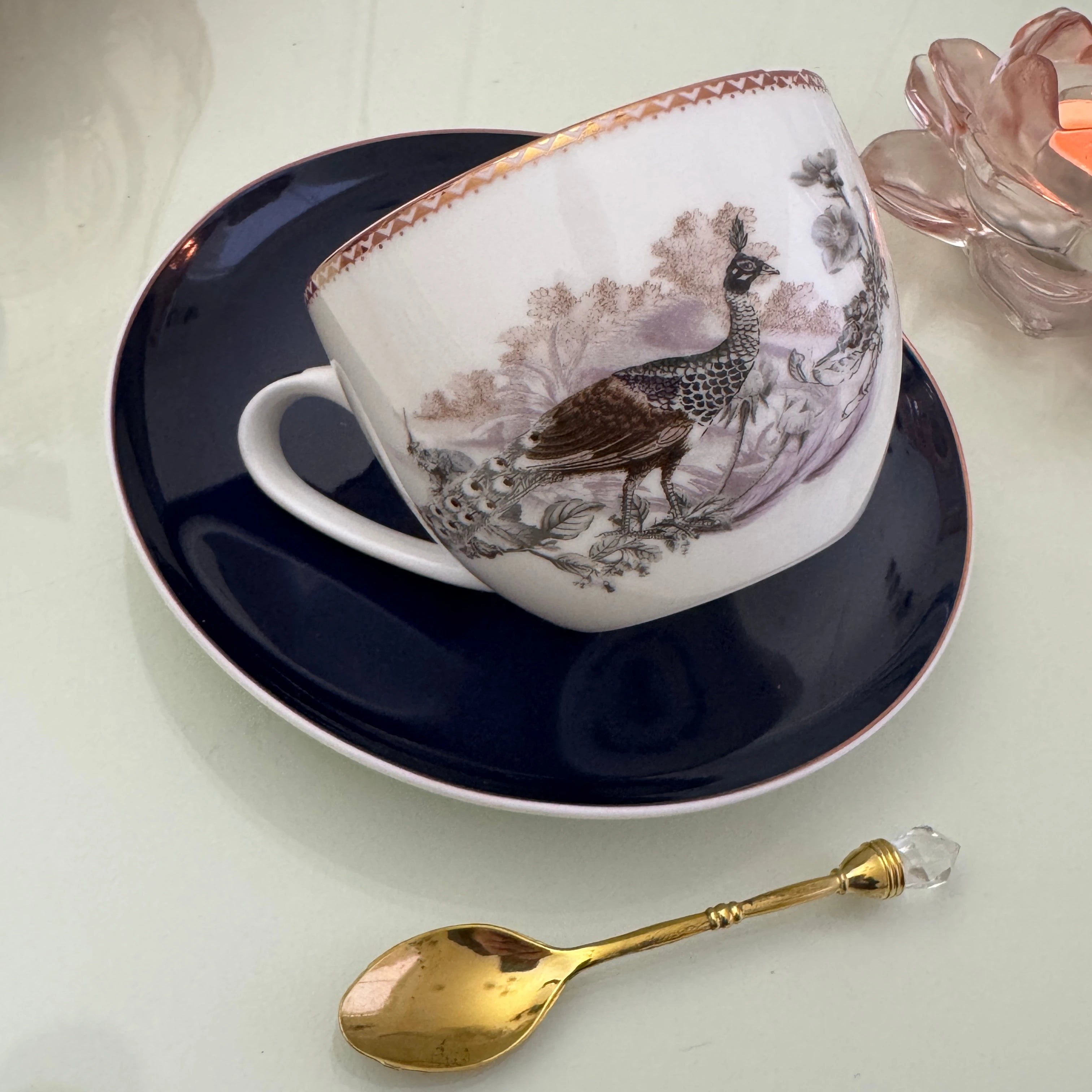 Right side view of peacock navy blue tea leaf reading teacup tilted on matching saucer with Tea With Karin stamp visible on base