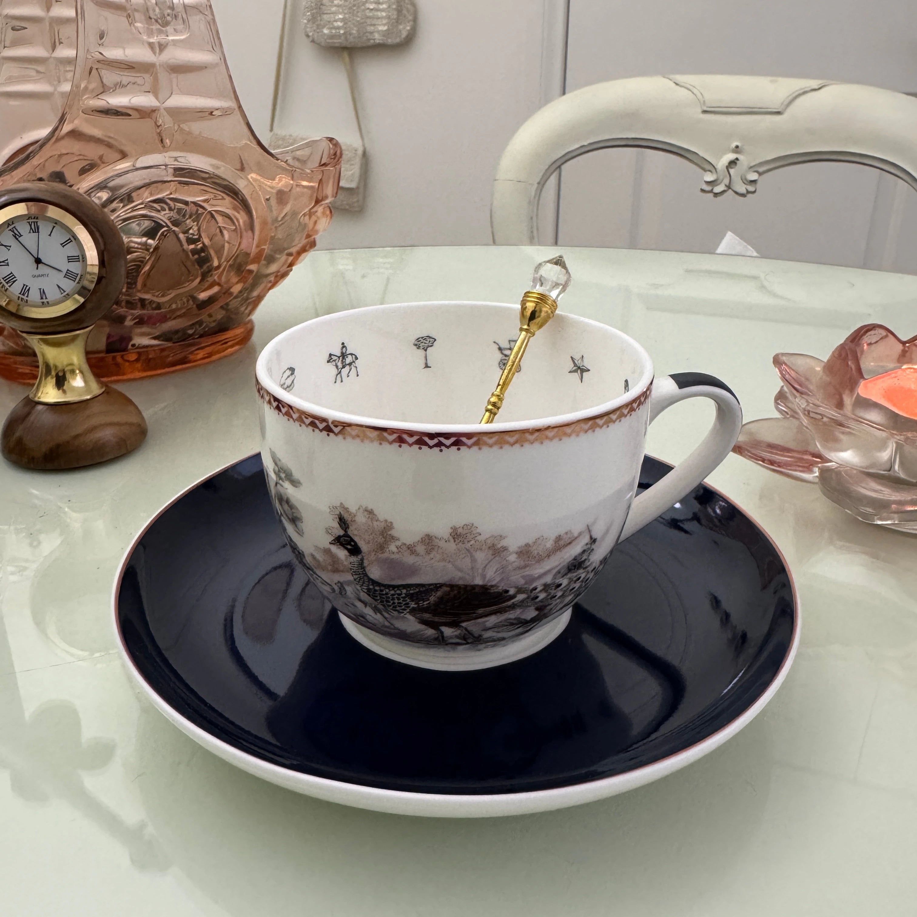 Peacock navy blue tea leaf reading teacup and saucer set with gold crystal teaspoon resting in cup, upright view showing divination symbols inside