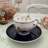 Peacock navy blue tea leaf reading teacup and saucer set with gold crystal teaspoon resting in cup, upright view showing divination symbols inside