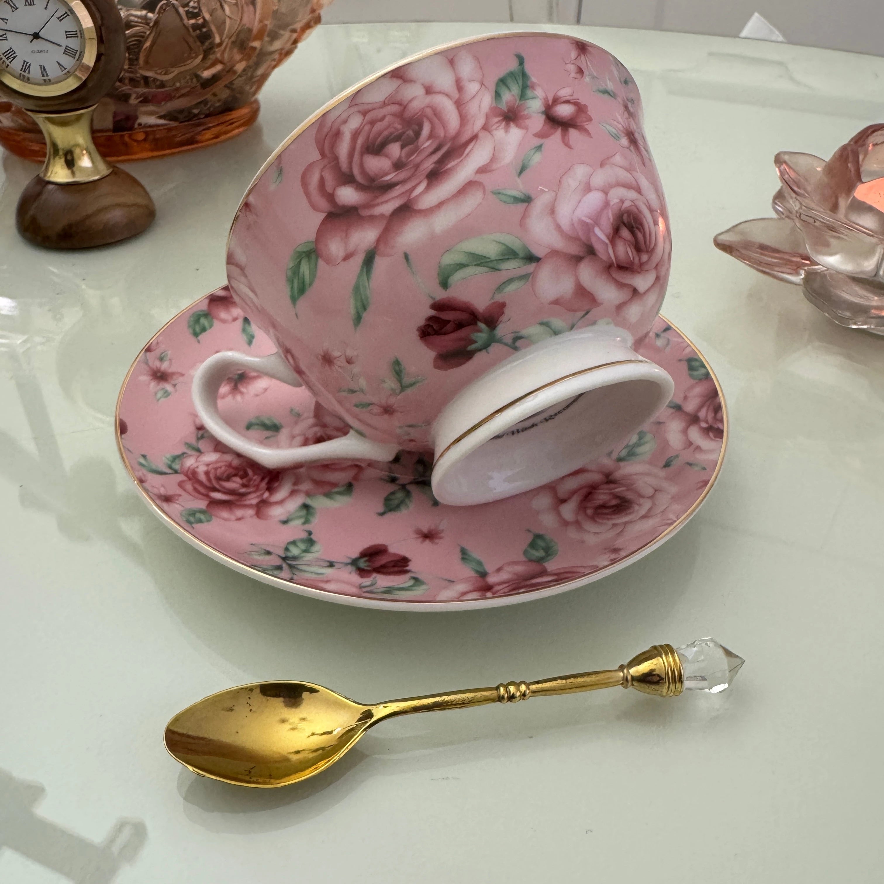 Right side view of pink rose floral tea leaf reading teacup resting on matching saucer with gold crystal teaspoon