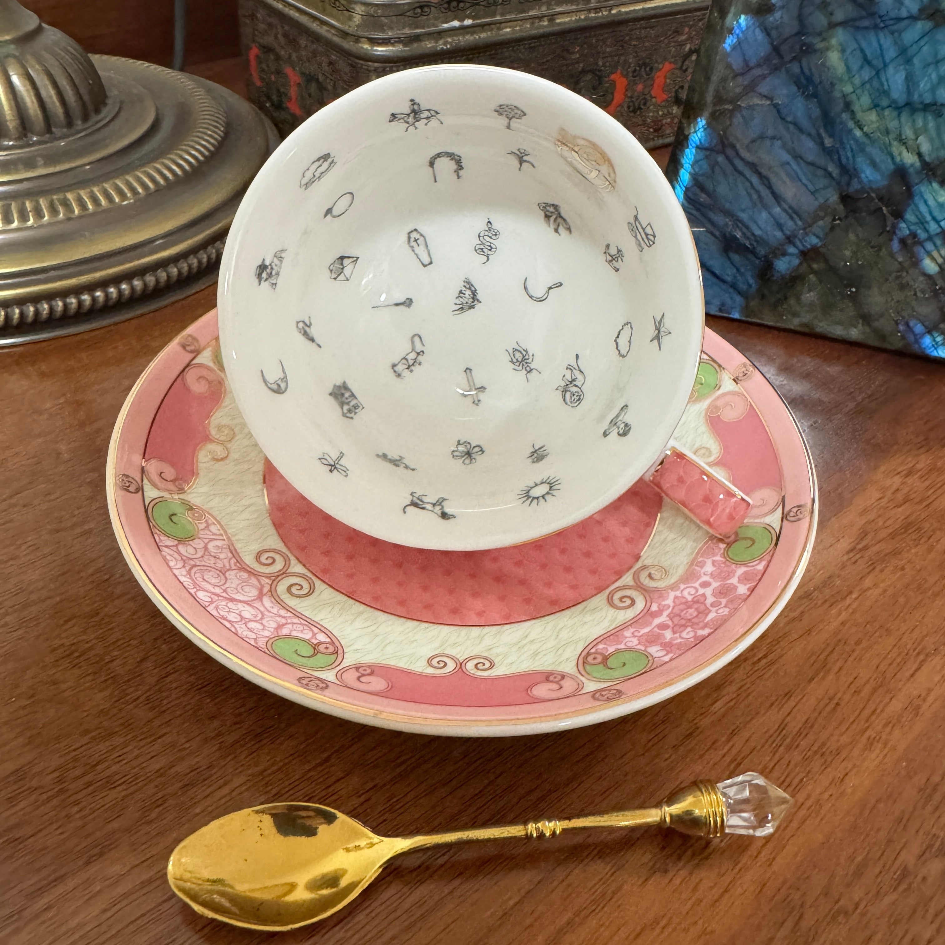 Teacup with decorative saucer and gold spoon on a wooden surface