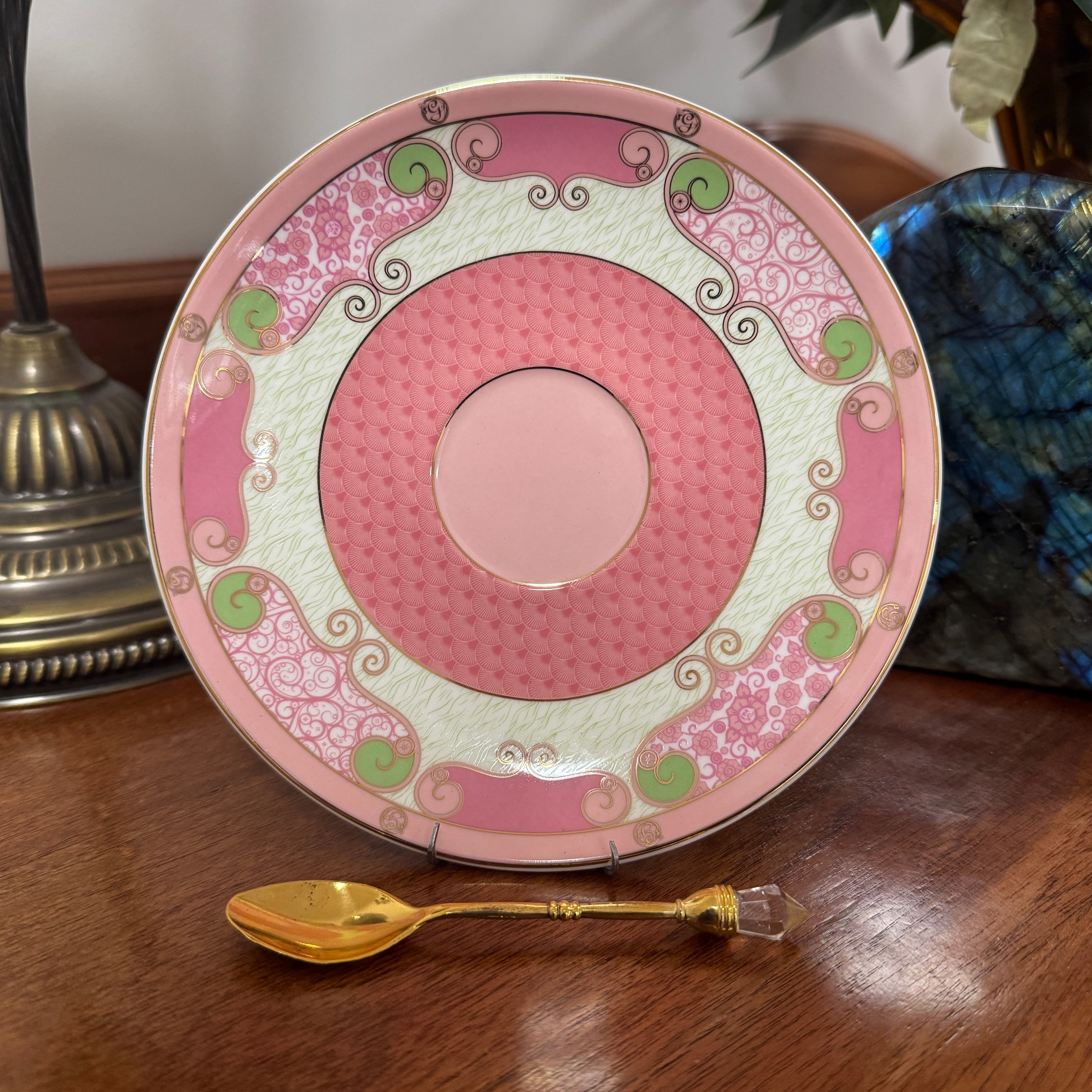 Decorative plate with pink and green patterns on a wooden surface with a gold spoon.
