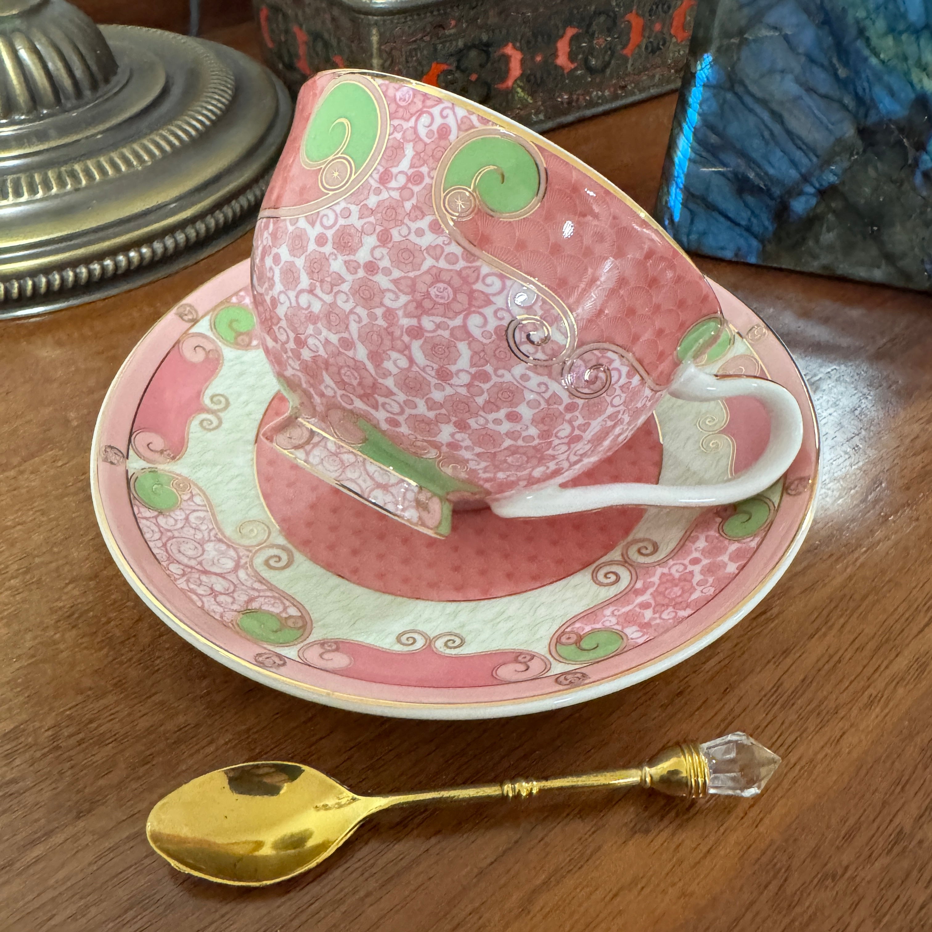 Teacup with vintage-style illustration, gold spoon, and decorative items on a white background