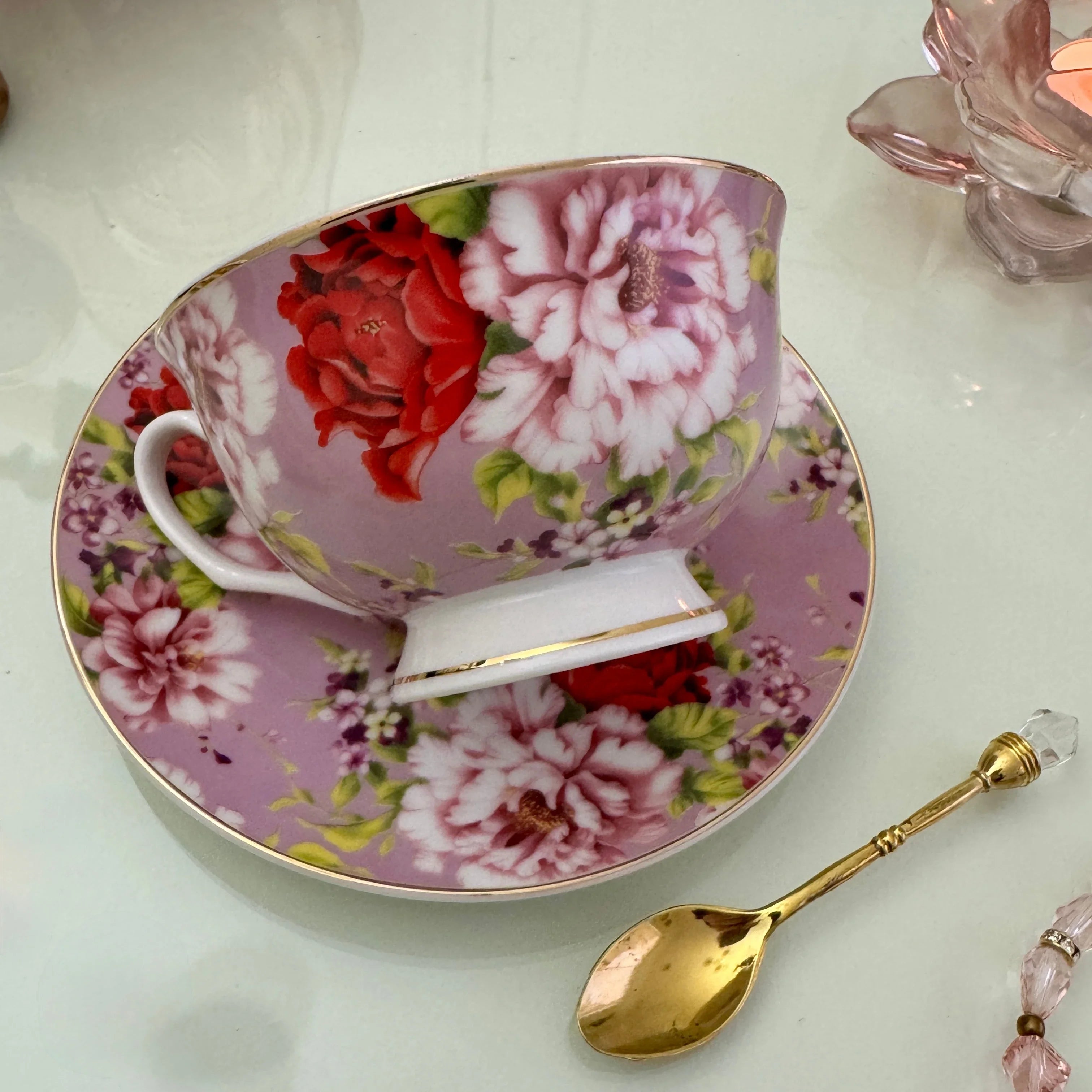 Right side view of pink red rose floral tea leaf reading teacup tilted on matching saucer with Tea With Karin stamp visible on base