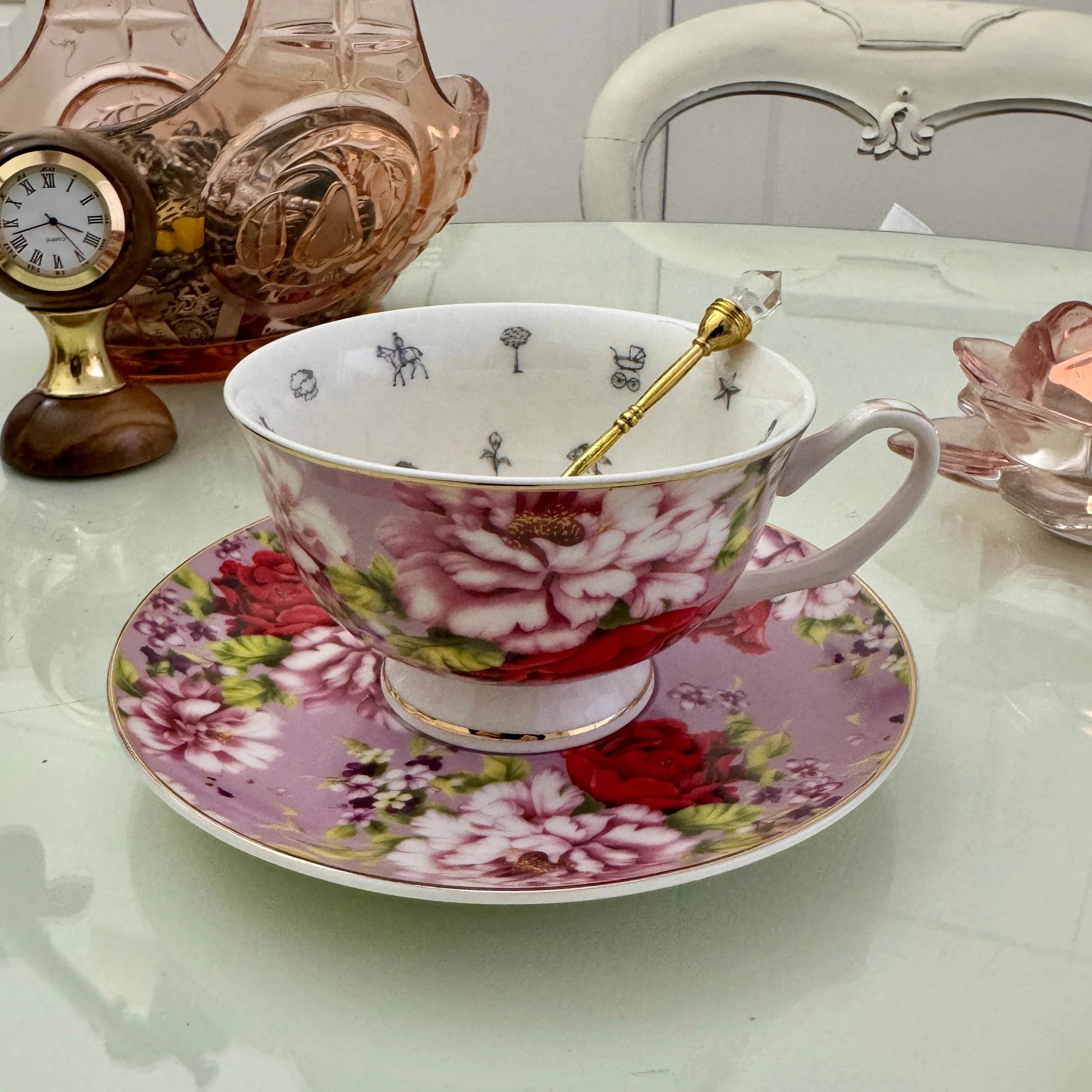 Pink red rose floral tea leaf reading teacup and saucer set with gold crystal teaspoon resting in cup, upright view showing divination symbols inside