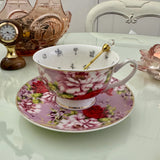 Pink red rose floral tea leaf reading teacup and saucer set with gold crystal teaspoon resting in cup, upright view showing divination symbols inside